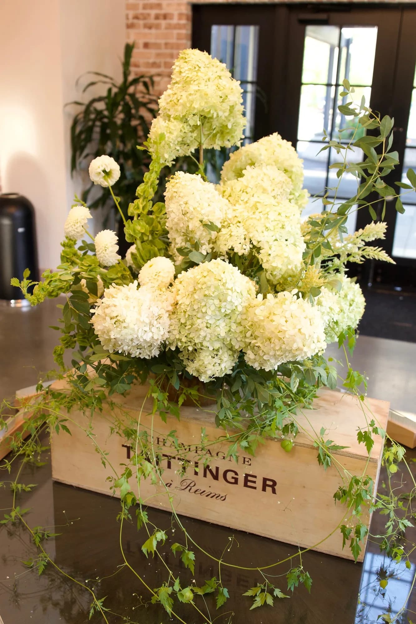Limelight hydrangea, white dahlias and bells of Ireland rise from a wooden crate, vine trailing across the dark tabletop