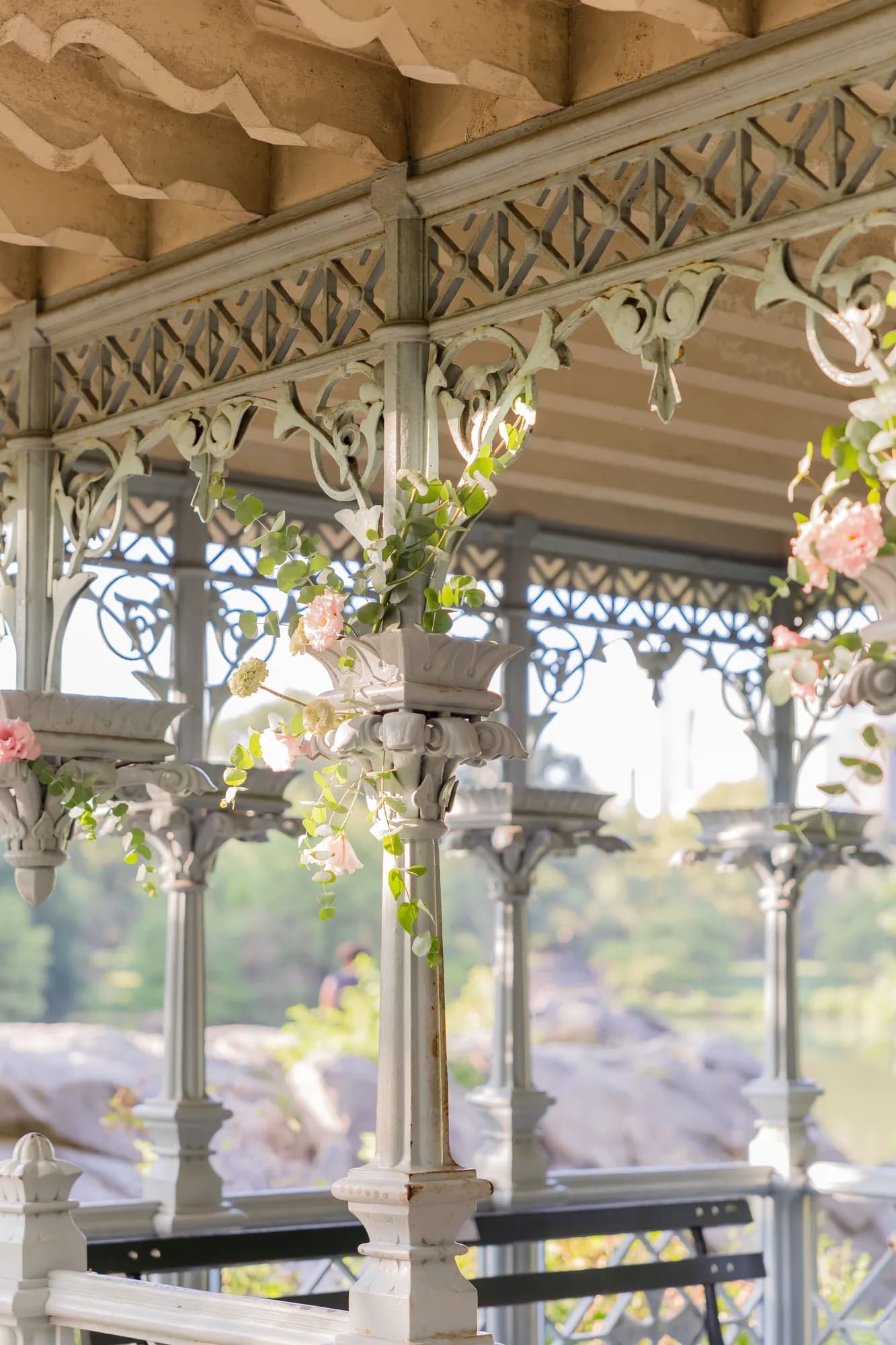 Eucalyptus and blush lisianthus trail from the capital of a slender cast-iron column beneath ornate pavilion fretwork