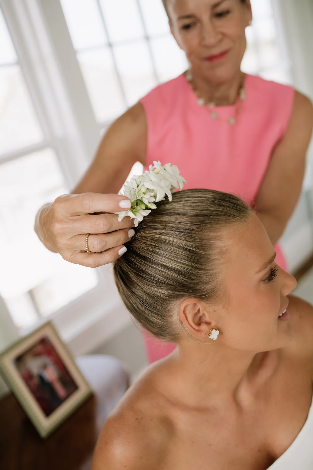 Close view of hands pinning a cluster of white tweedia blossoms into the back of Lindsey's low chignon