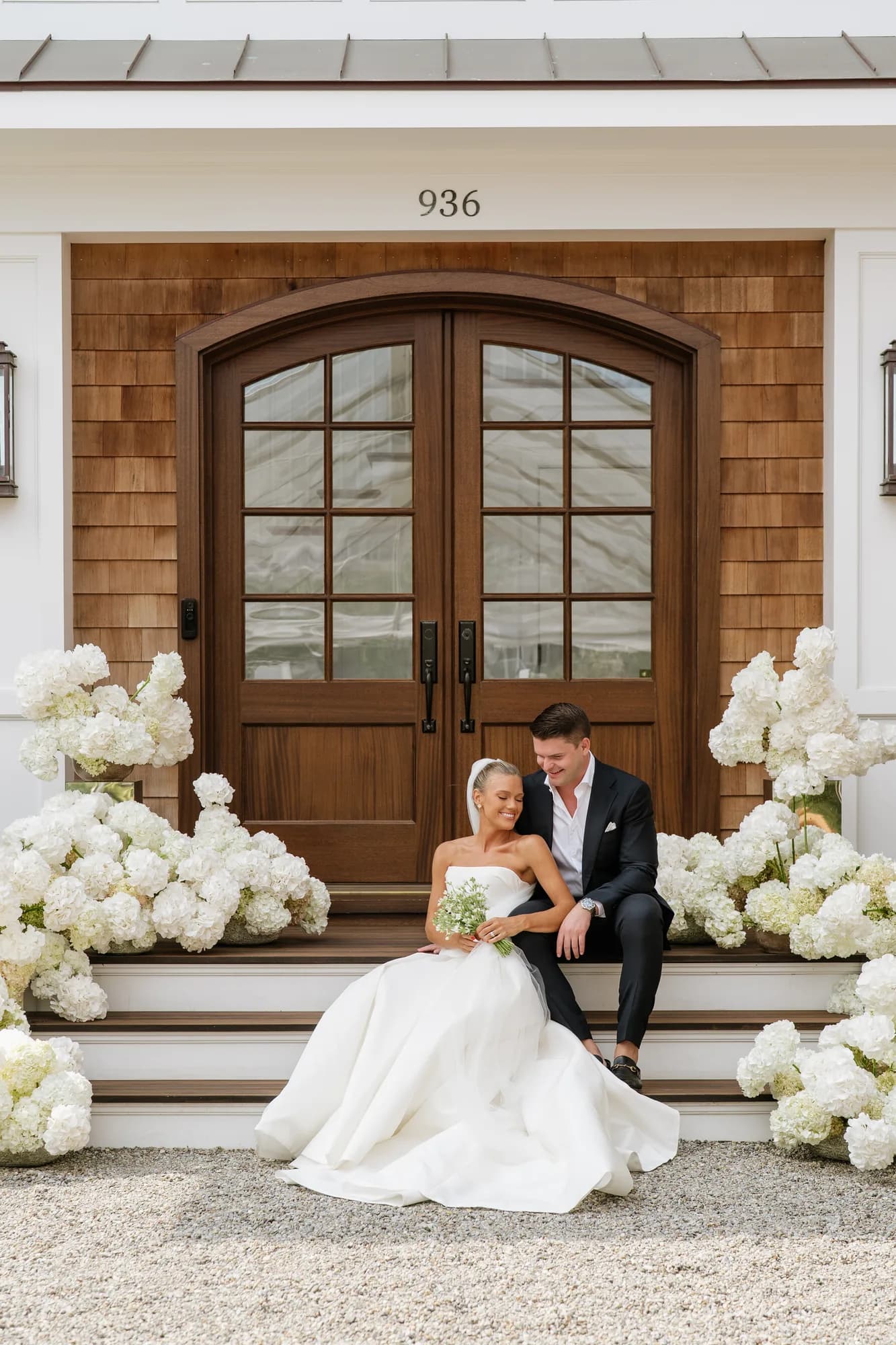 Lindsey and Finn seated on the front steps, white hydrangea massed in drifts on either side of the arched doors