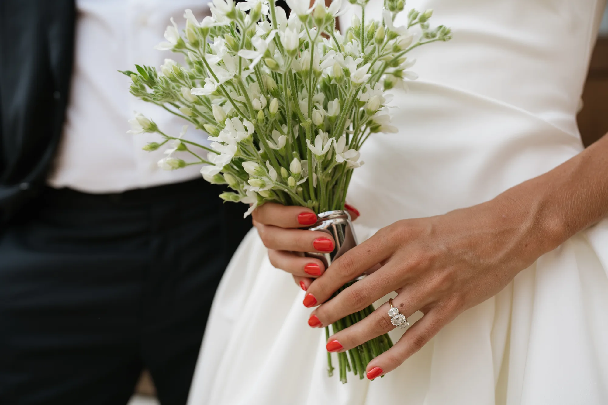 Lindsey's hands around her tweedia bouquet, the stems bound in a polished silver cuff, red nails against green