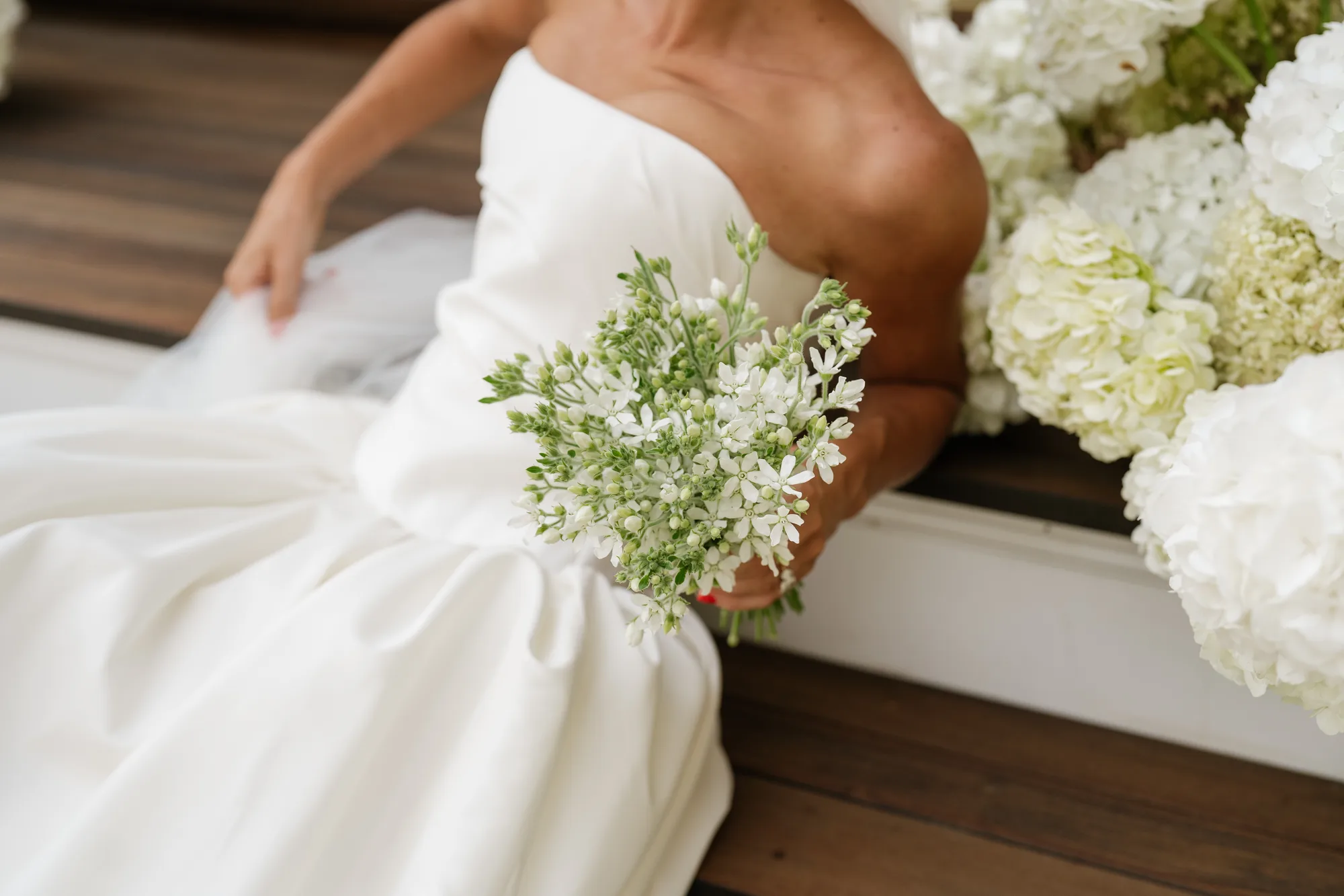 Lindsey seated on the steps with her tweedia bouquet in hand, white hydrangea heads gathered beside her