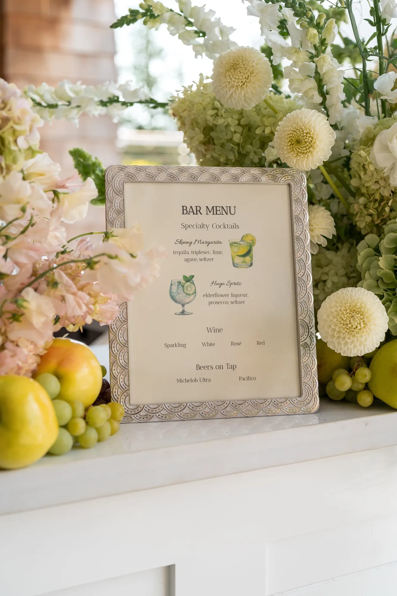 A framed bar menu set among blush sweet pea, cream pompon dahlias, limelight hydrangea, grapes and apples