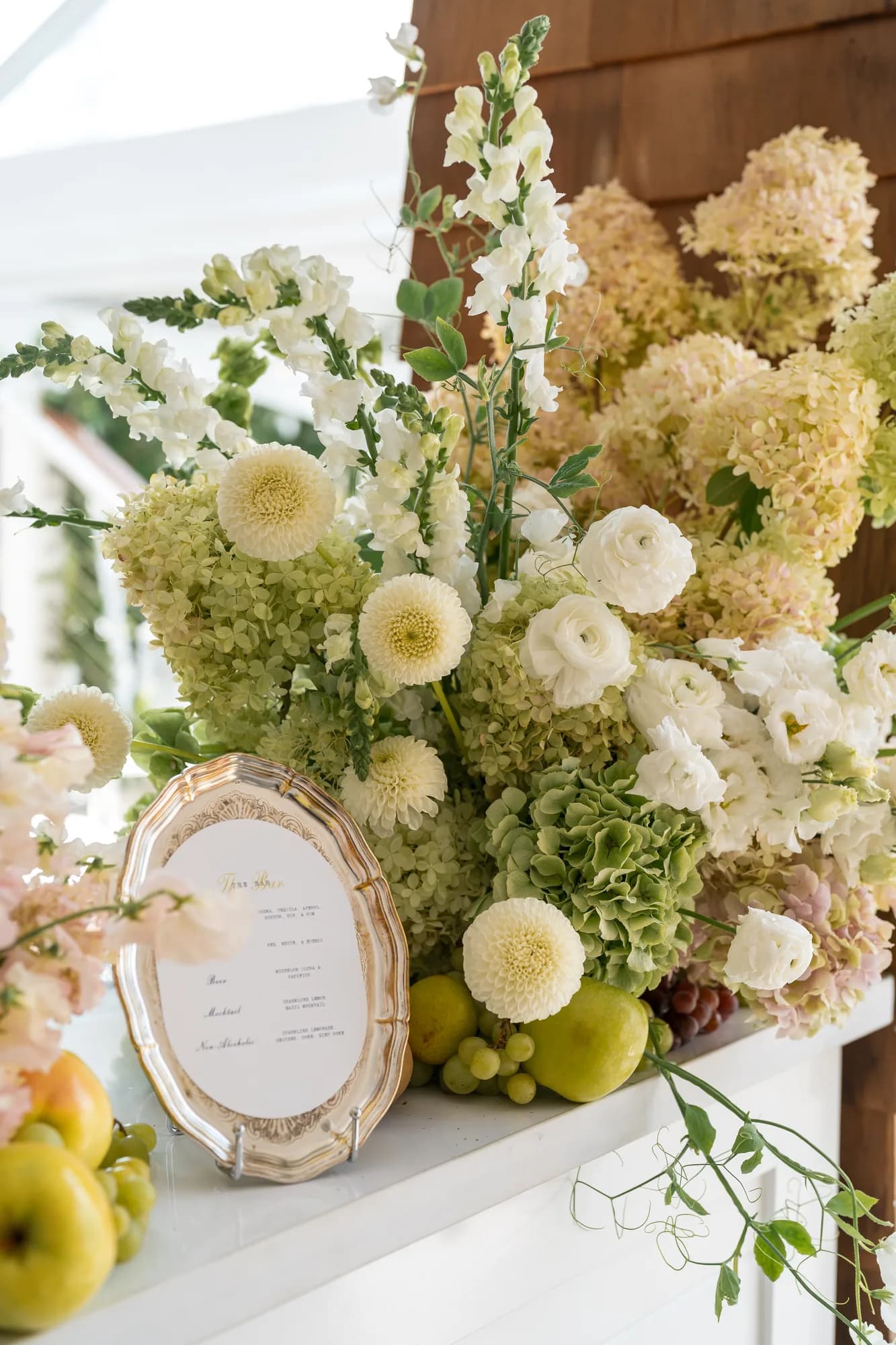 Cream pompon dahlias, white snapdragon and ranunculus rise above limelight hydrangea beside a silver menu tray