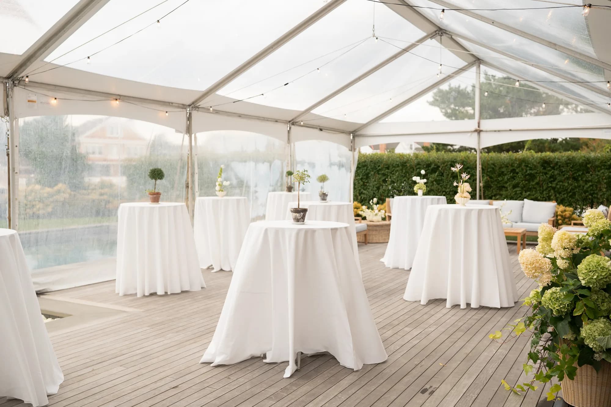 Cocktail tables under a clear tent by the pool, each with a single small topiary or ikebana-style arrangement
