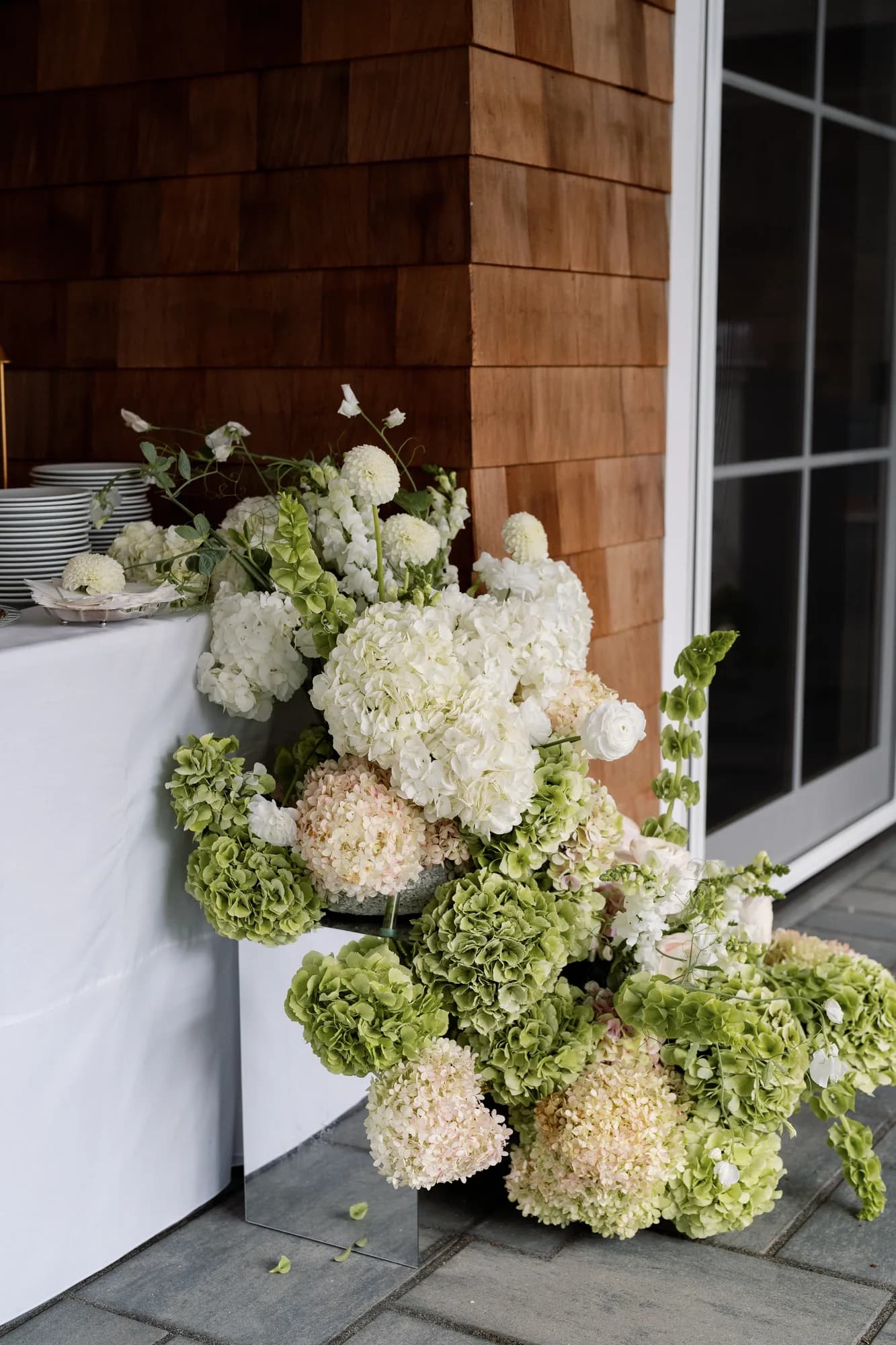 A cascading arrangement of green and white hydrangea, dahlias and bells of Ireland at the corner of the buffet