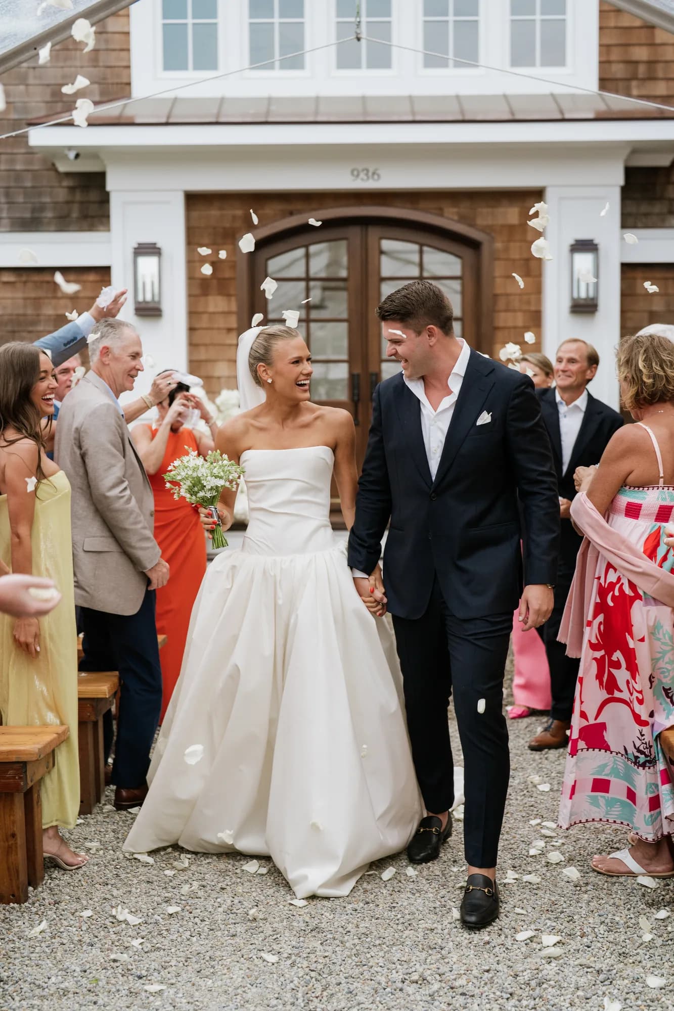 Lindsey and Finn walk hand in hand up the aisle through falling white petals, guests standing at the benches