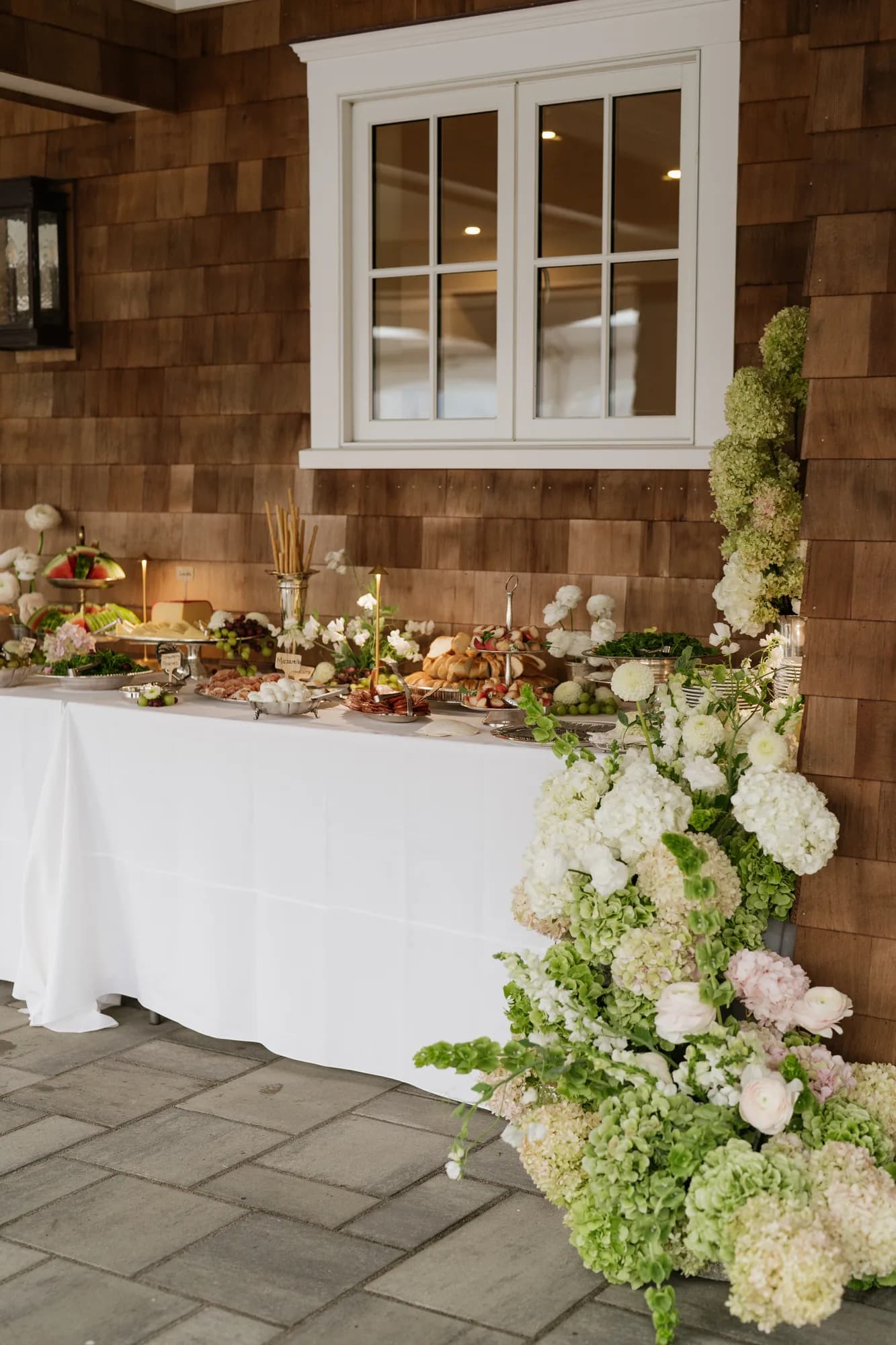 A long buffet in the breezeway with a cascading arrangement of hydrangea, ranunculus and bells of Ireland at its end