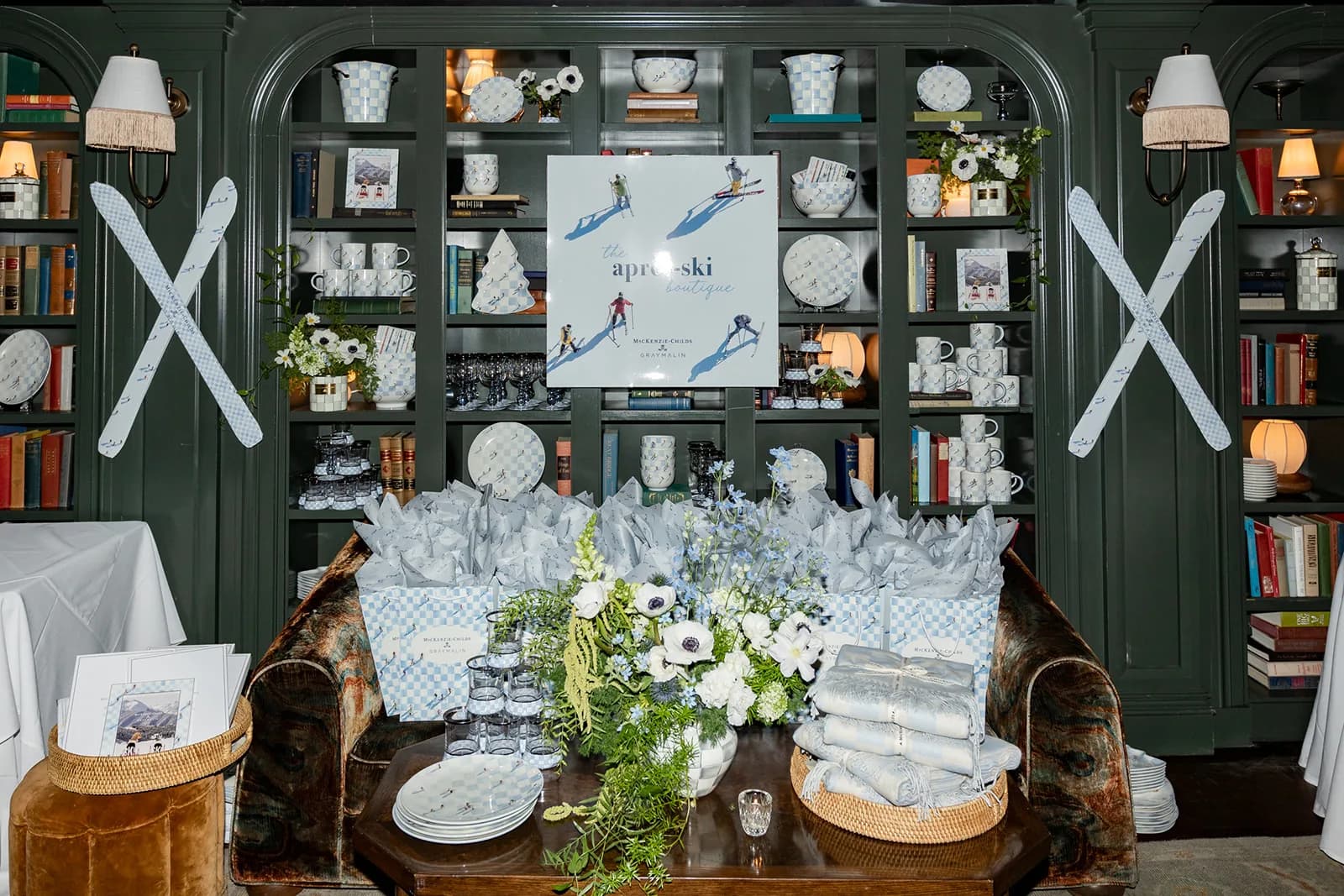 Gift bags and a low arrangement of anemones and blue delphinium fill a velvet sofa below the après-ski boutique sign
