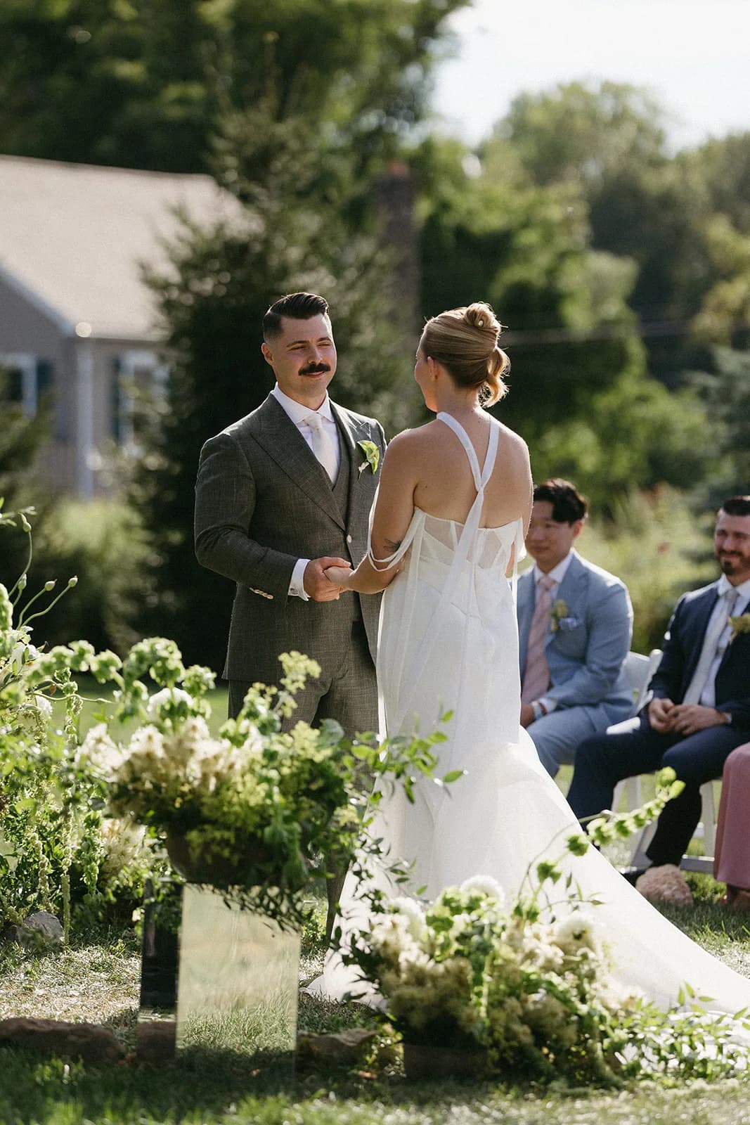 Groom holds the bride's hands, a deconstructed arrangement of bells of Ireland and Phylica on a mirrored plinth beside them