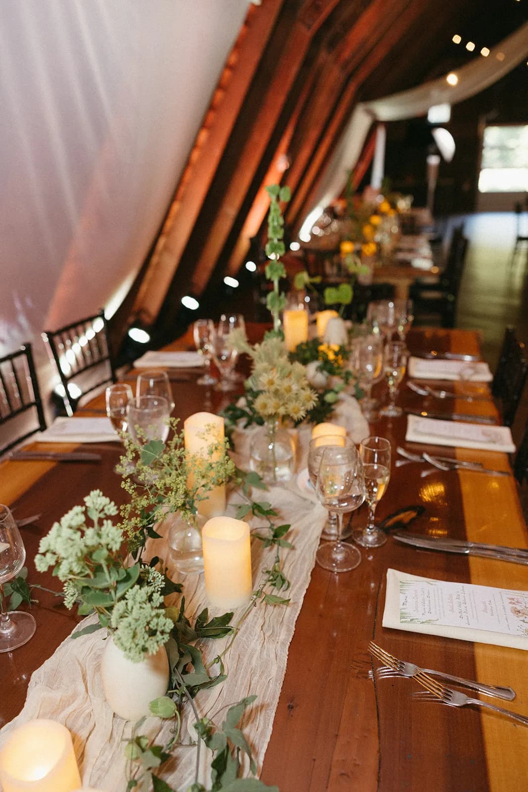 Long tablescape with a gauze runner, pillar candles, and bud vases of sedum, lady's mantle, Phylica, and bells of Ireland