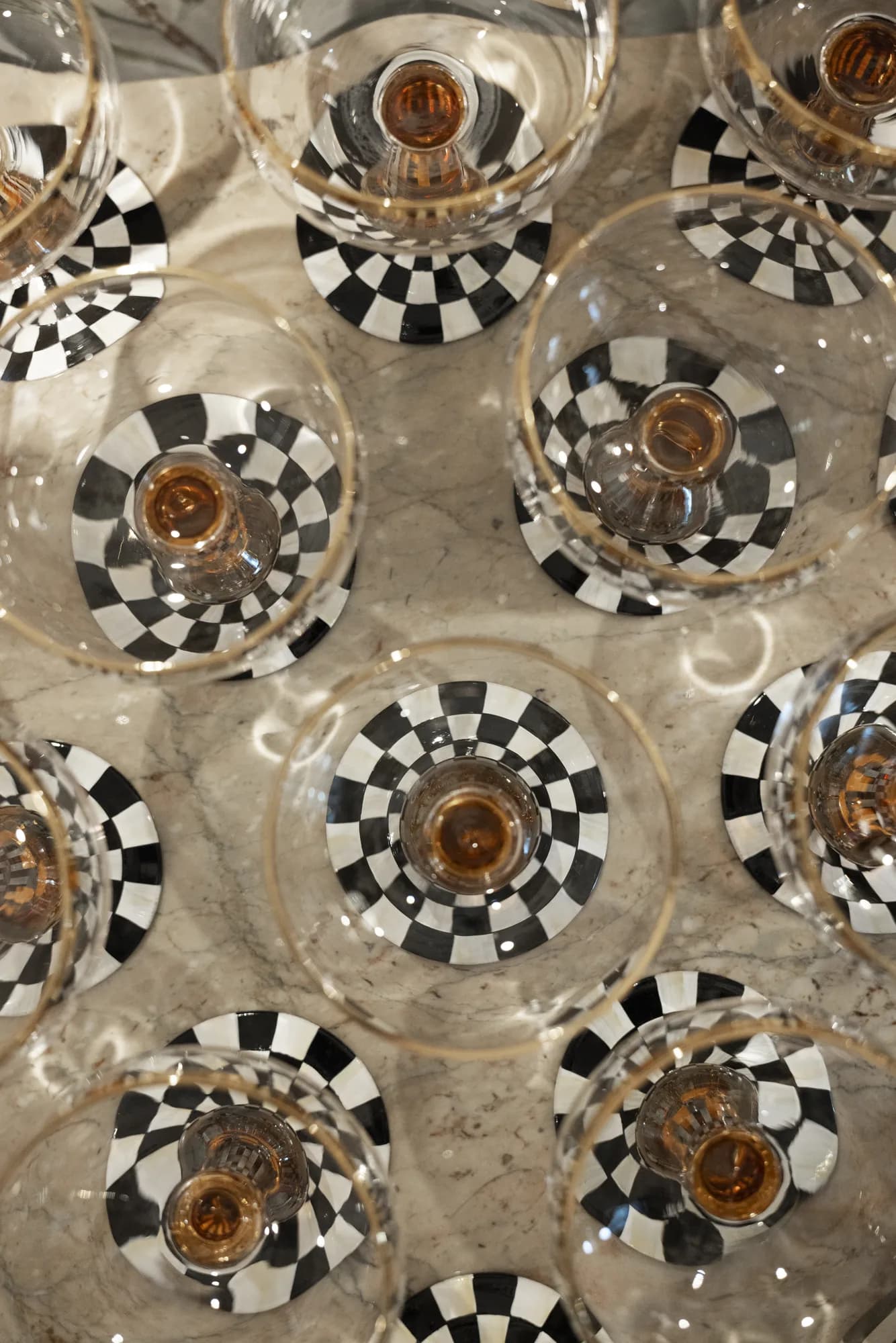 Overhead view of amber-stemmed coupes with black and white check bases clustered on a marble counter