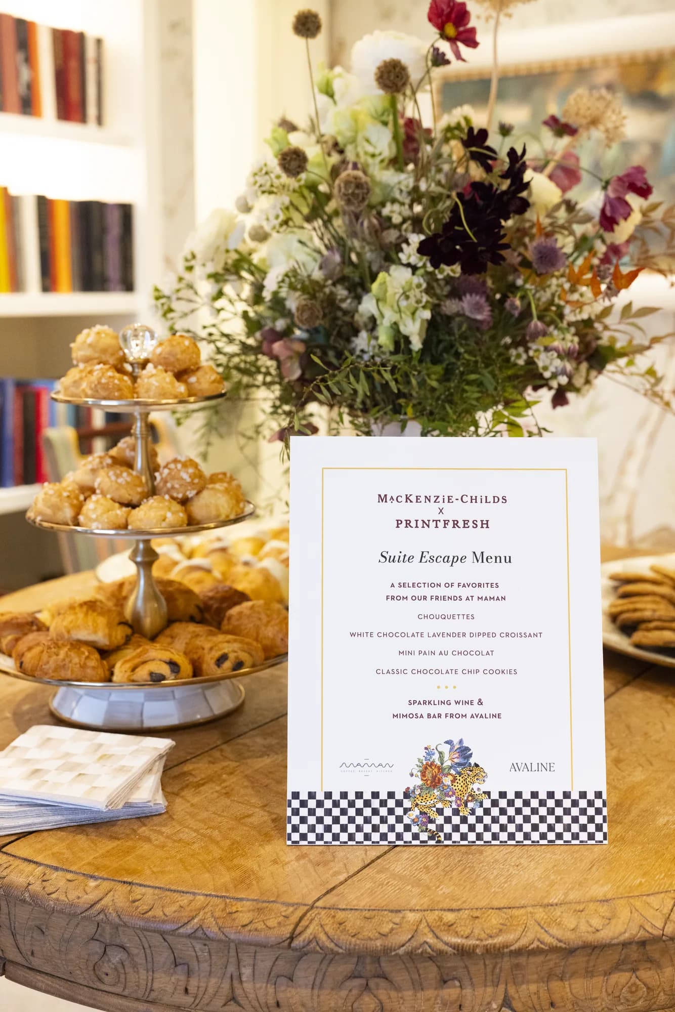 Tall loose arrangement of ranunculus, chocolate cosmos and dried allium behind a MacKenzie-Childs x Printfresh menu card