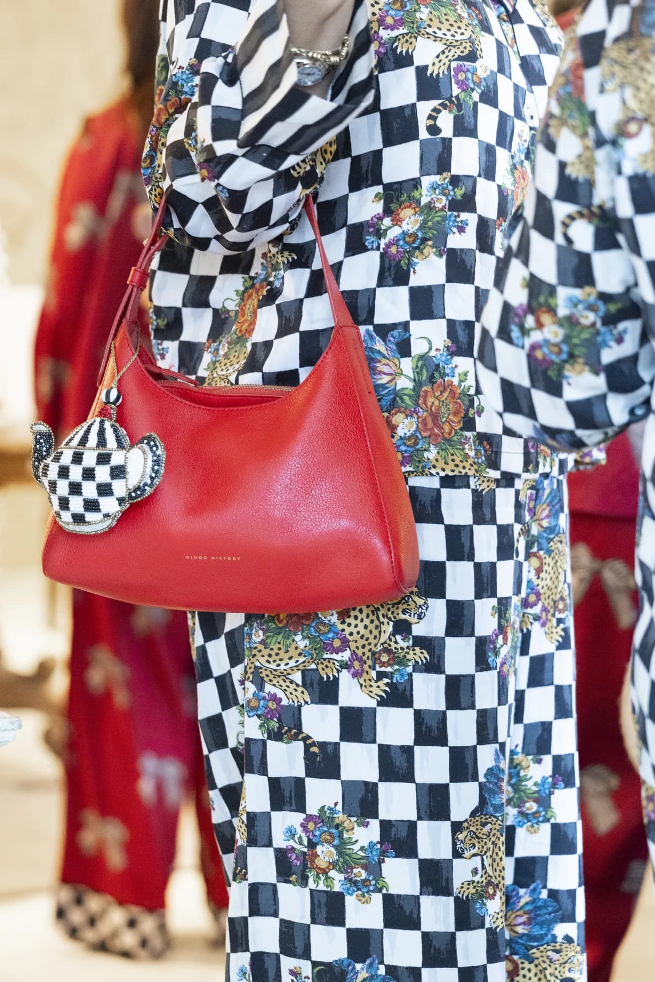 Detail of a red leather bag with a beaded check teapot charm against checkered leopard-print Printfresh pajamas
