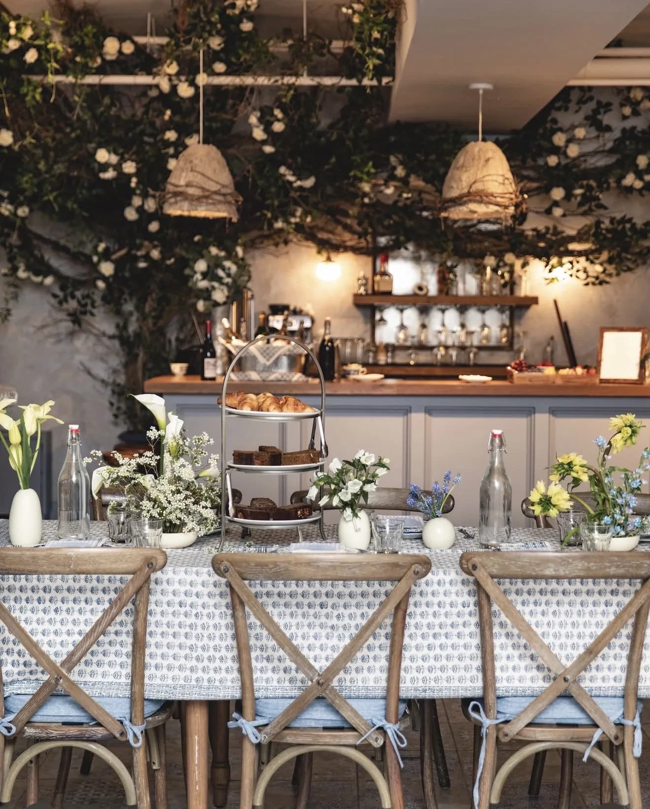 Vine and white rose canopy trails over pendant lamps above a long brunch table set with bud vases of calla lilies and tulips