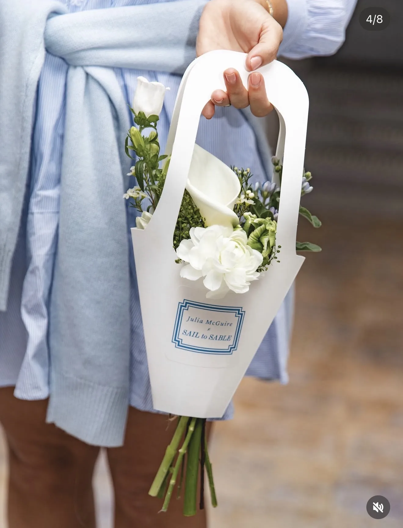 Guest holds a Sail to Sable paper carrier with a small posy of calla lily, ranunculus, waxflower and agapanthus buds