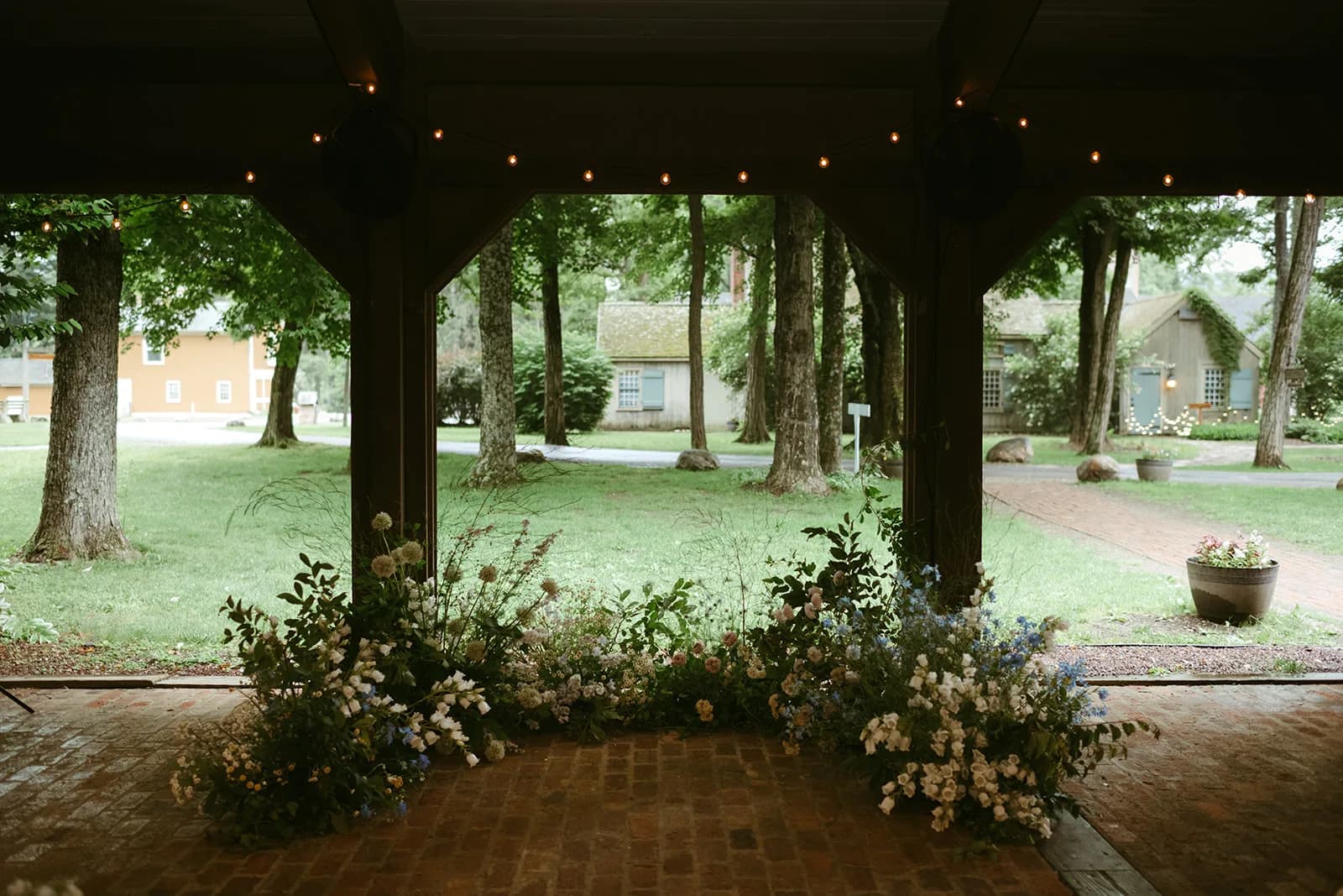Crescent installation of white campanula, allium, blue delphinium and strawflower edges a brick pavilion floor open to lawn