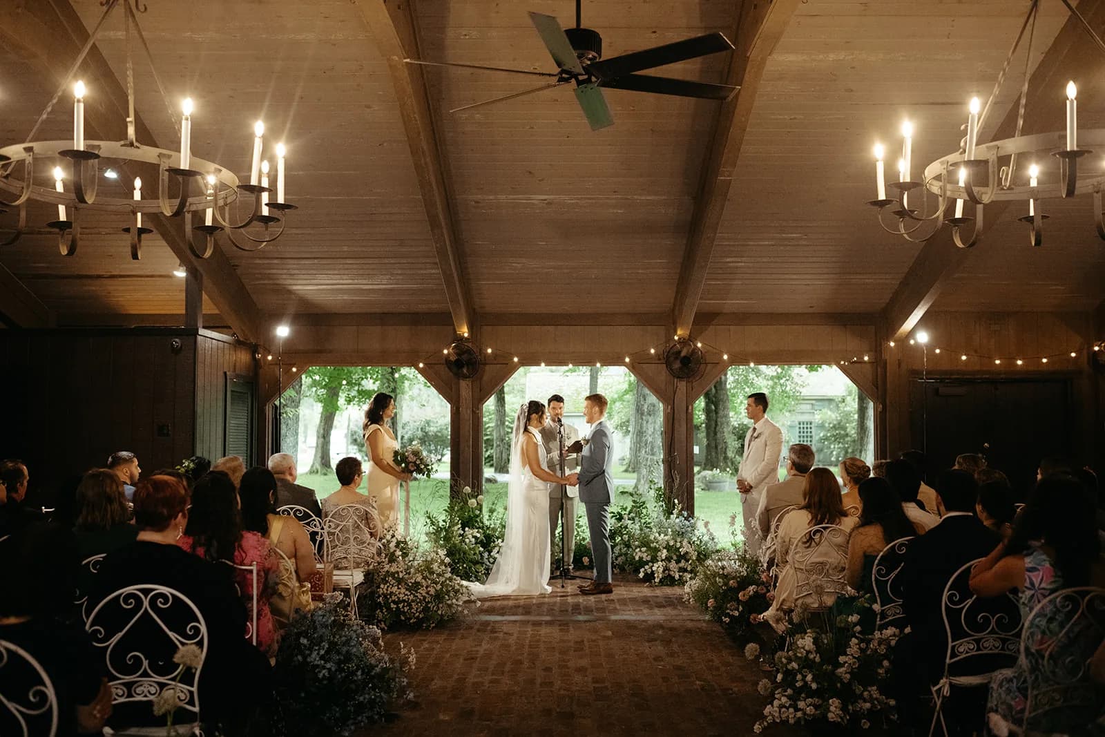 Wide view down the brick aisle as guests watch the ceremony, low banks of white and blue blooms lining the chairs