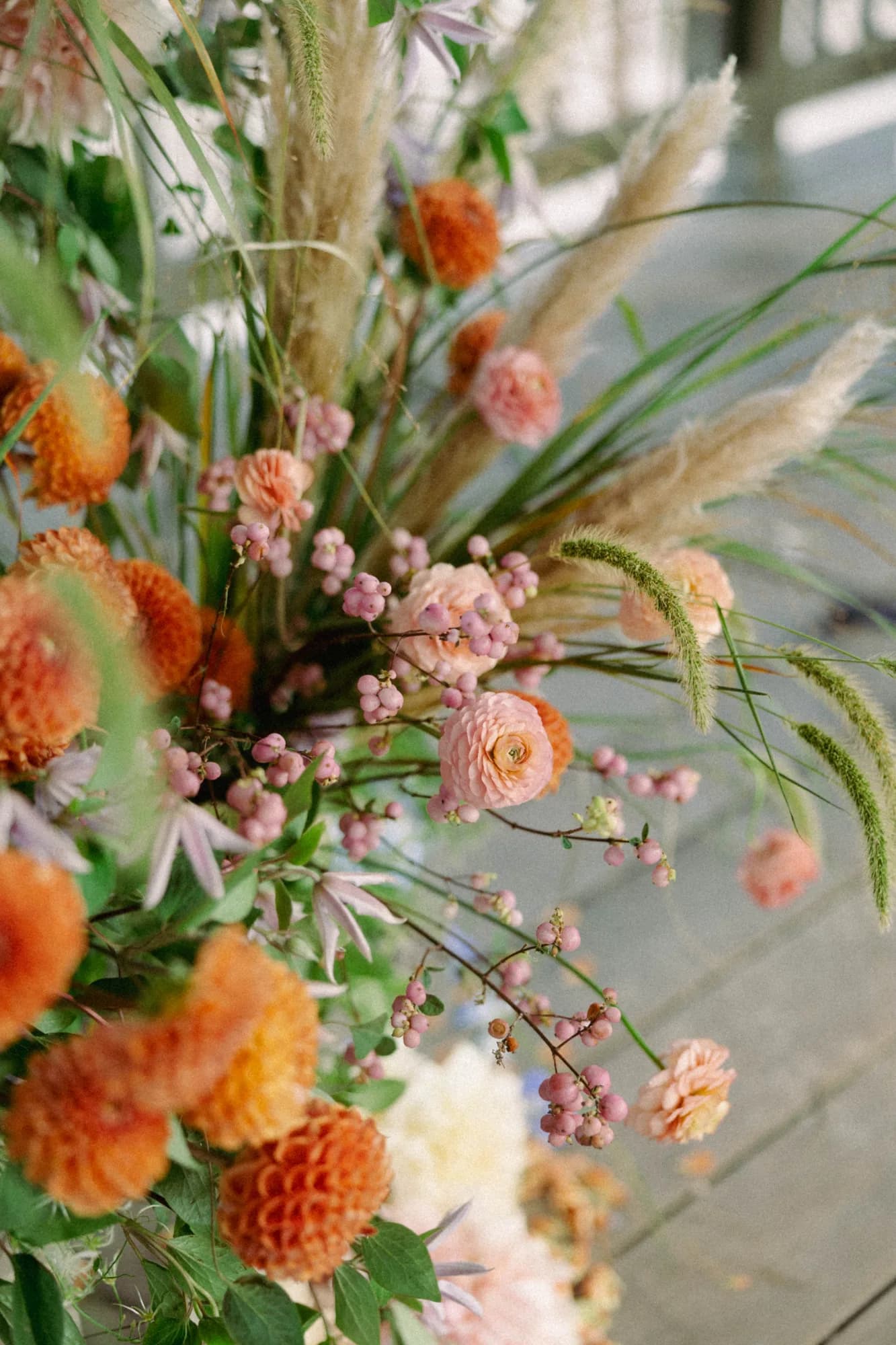 Detail of orange dahlias, pink ranunculus, snowberry and pampas grass in a ceremony arrangement on a weathered deck