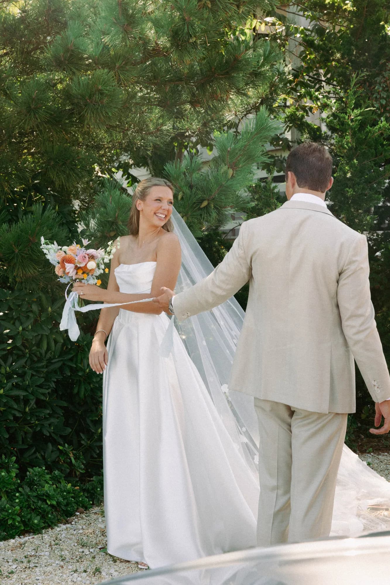 Talea laughs as Erich holds her veil, her bouquet of orange dahlias and clematis tied with pale blue ribbon