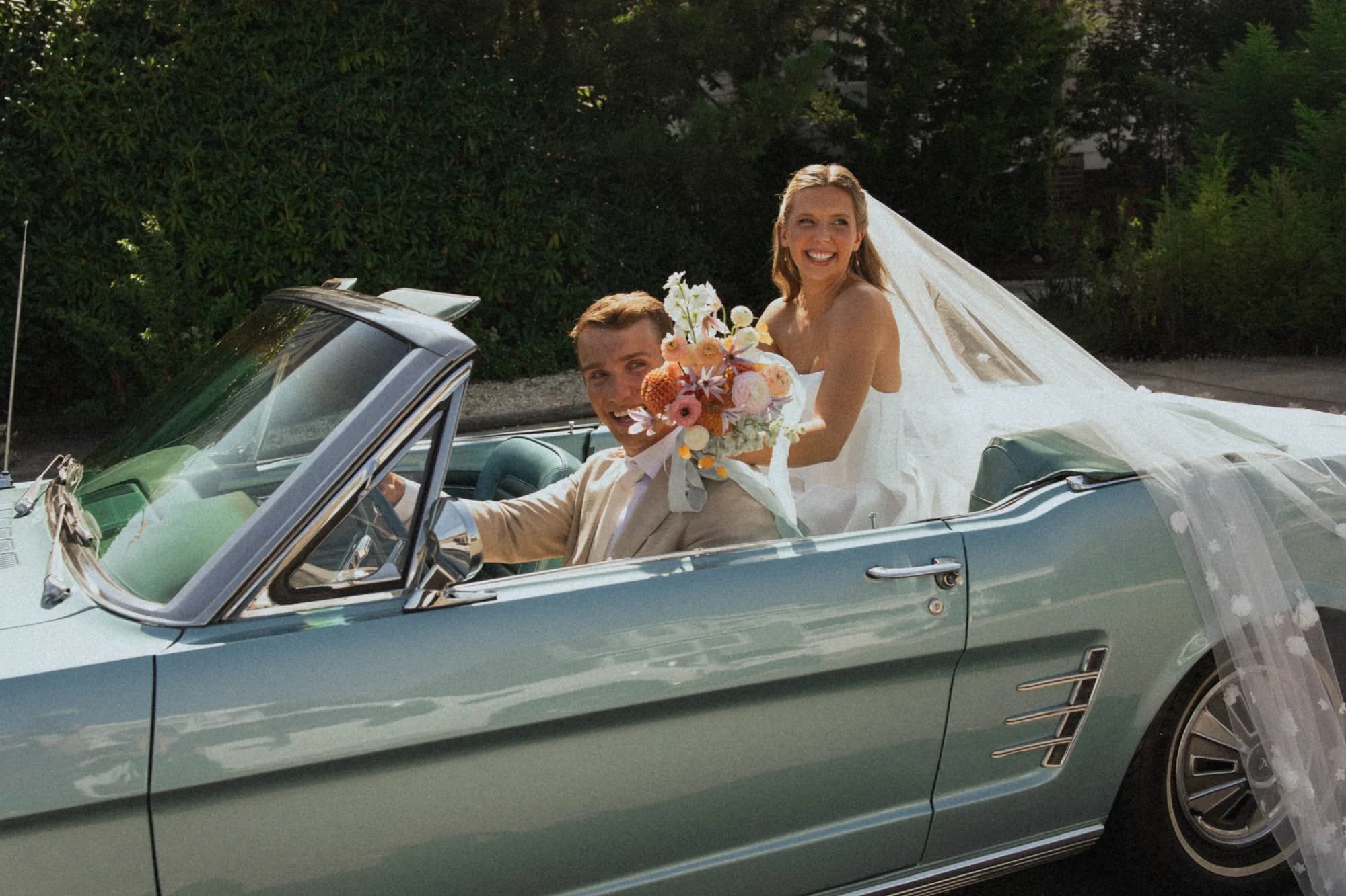 Talea and Erich in a pale blue convertible, her bouquet of orange dahlias and clematis held beside him