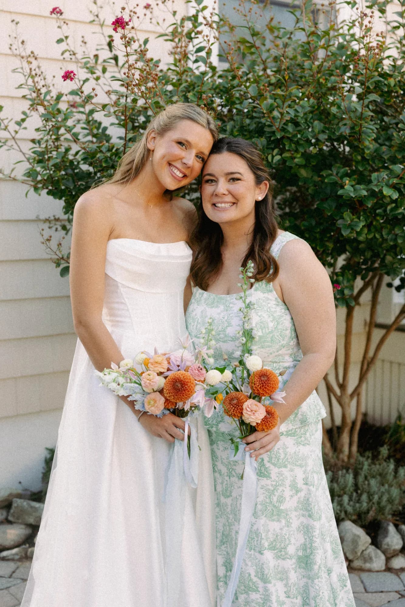 Talea and a bridesmaid hold bouquets of orange dahlias, peach ranunculus and clematis tied with pale blue ribbon
