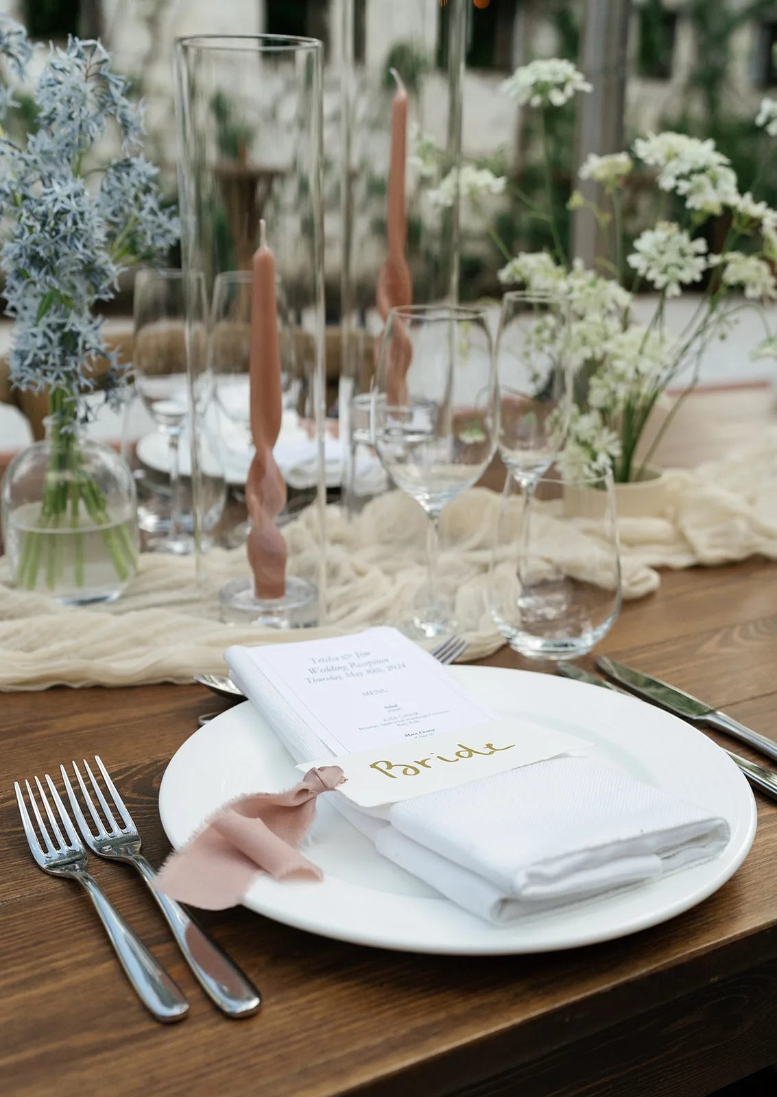 Trisha's place setting with a menu tucked in the napkin under blush silk ribbon, twisted tapers and pale blue amsonia behind