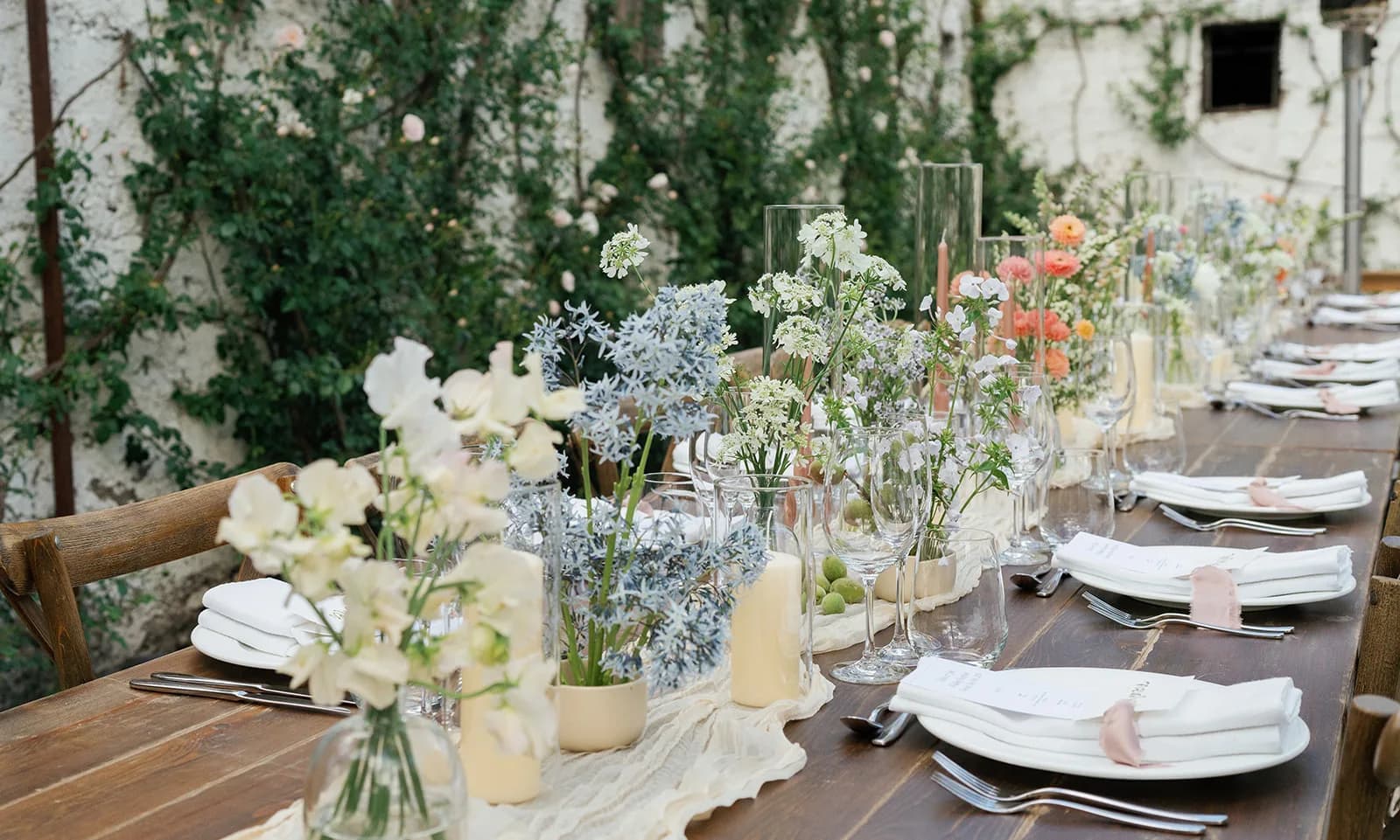 Low view down the tablescape, white sweet pea and pale blue amsonia in front, lace flower, ranunculus and baby peaches beyond