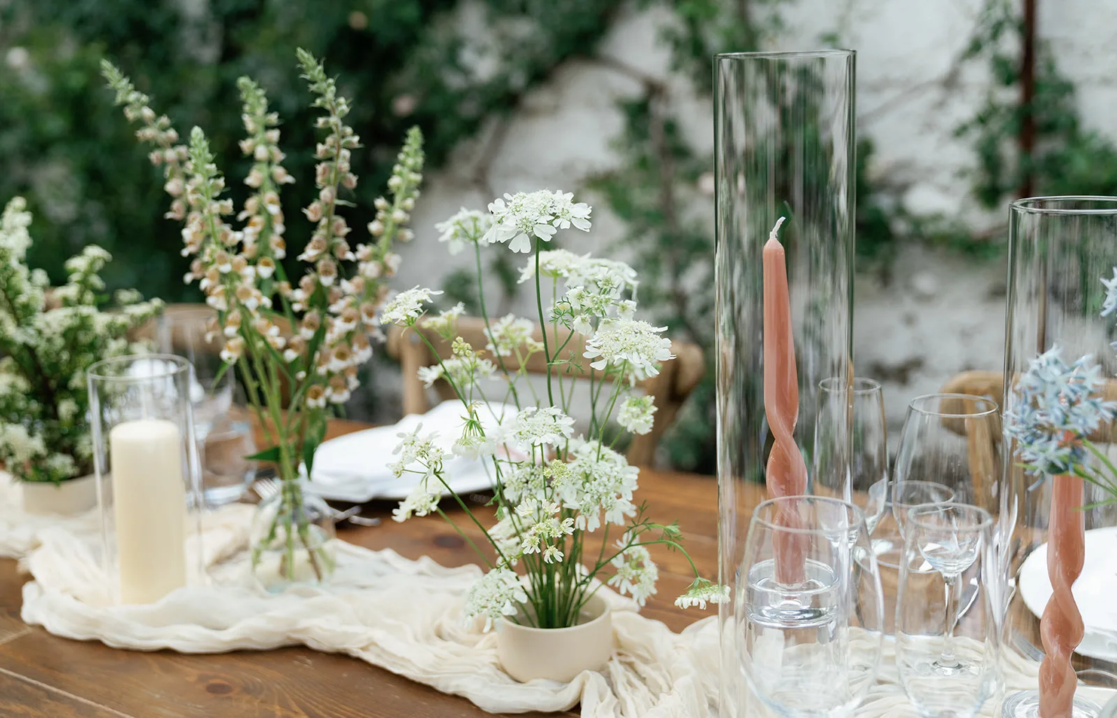 Foxglove, white lace flower and twisted blush tapers in tall glass hurricanes compose one cluster of the reception tablescape