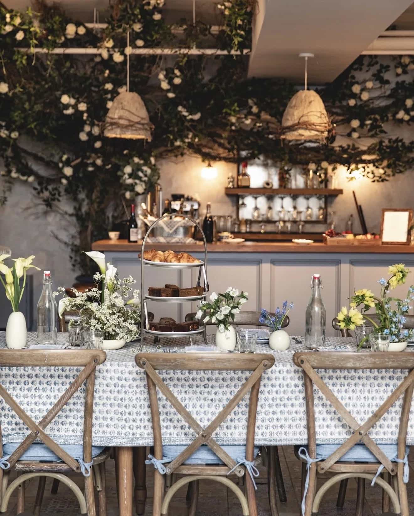 Vine and white rose canopy trails over pendant lamps above a long brunch table set with bud vases of calla lilies and tulips